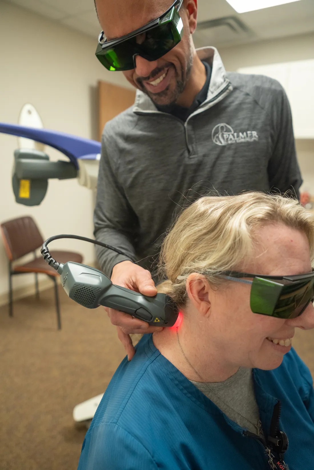 Dr. James Palmer applying a therapeutic laser to a patient's lower back while both wear protective eyewear